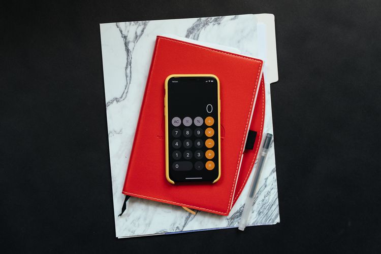 Image of an iPhone with the "calculator app" opened sitting on top of a notepad