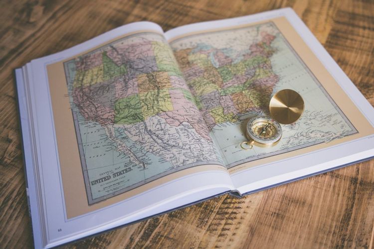 Image of an open book with a map of the united states on the page and a compass sitting on top of the book