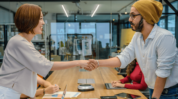 Image of a man and woman shaking hands sitting around a conference table.