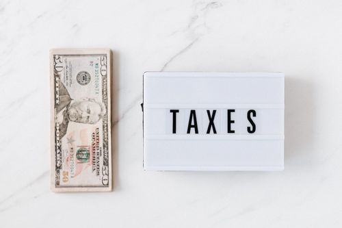 Image of a fifty dollar bill sitting on a countertop with a sign that says "taxes" on it