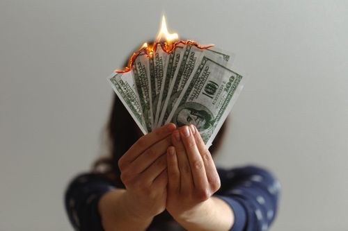 Image of a woman holding a fan of one hundred dollar bills that are on fire