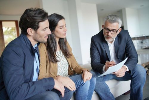 An image of a younger couple looking at a piece of paper that an older real estate agent is holding
