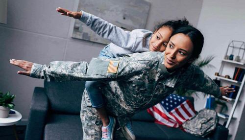 Image of a mother dressed in a military uniform with her daughter on her back